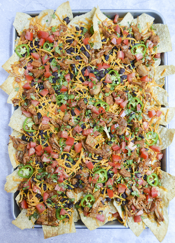 Loaded Vegan Nachos - these sheet pan nachos are loaded with shredded jackfruit, tomato, black beans, jalepeno and vegan cheese (or regular cheese--you pick!). #nachos #vegan #plantbased #recipe https://pumpsandiron.com